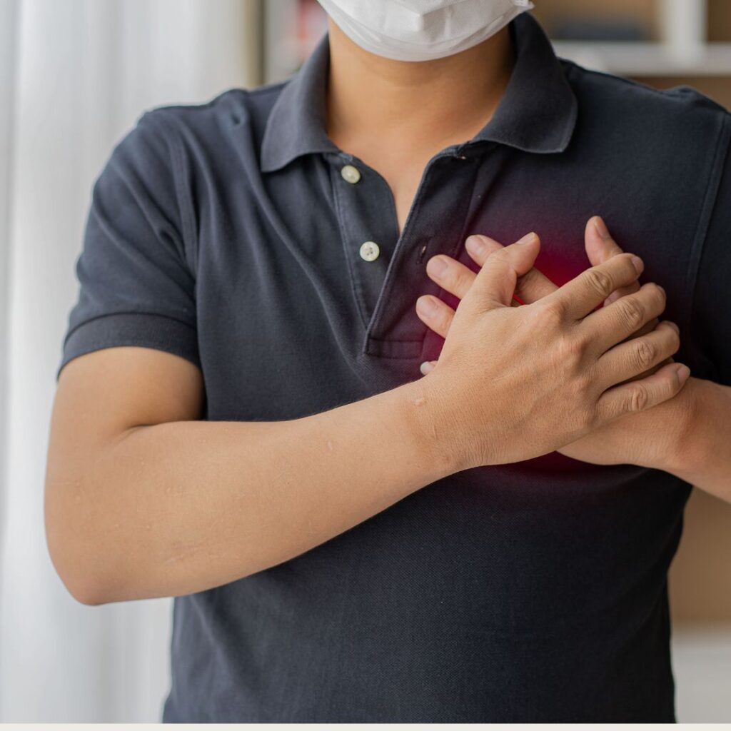 A person wearing a facemask in maroon holding his chest over his heart