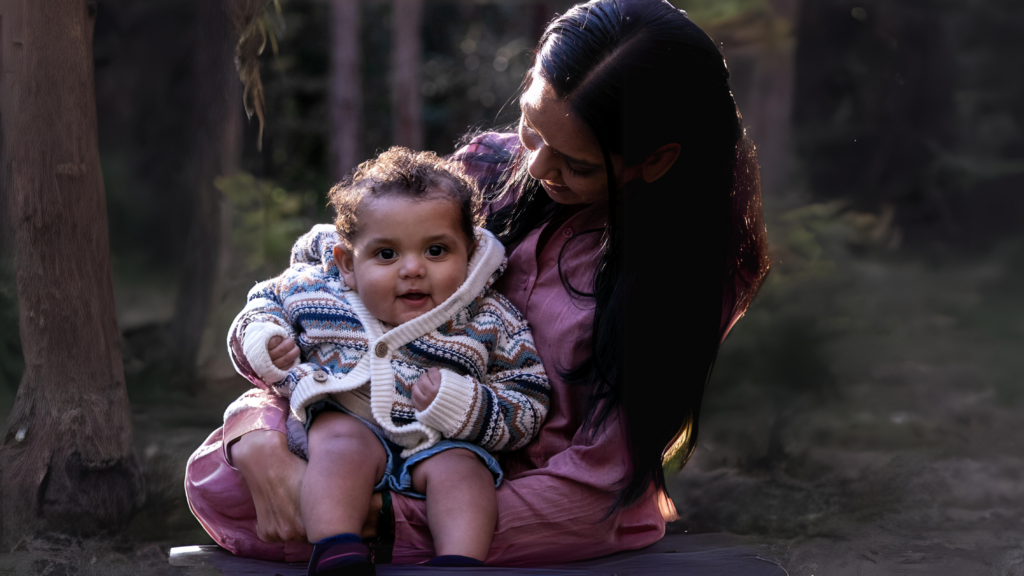 a mother holding her baby in a forest background with the sun lighting over their hair