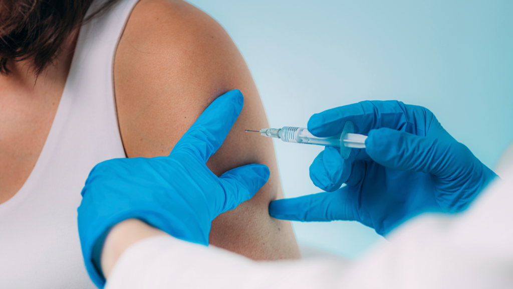 a medical professional hands injecting an immunisation on a person in white tops in her upper arm